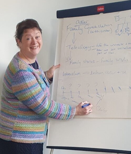 Annie wearing a multicoloured pastel cardigan writing on a flipchart and smiling at the camera.