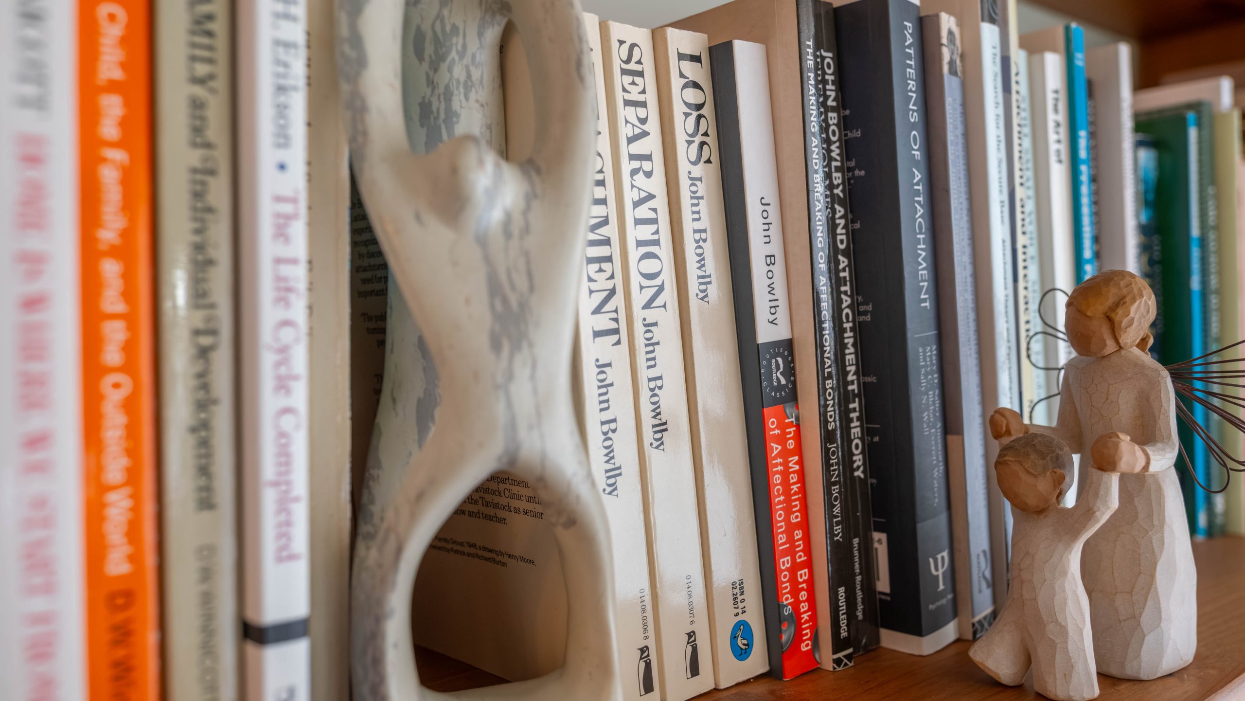Some books on Annie's shelf, and a figurine of an angel holding a child up and supporting them