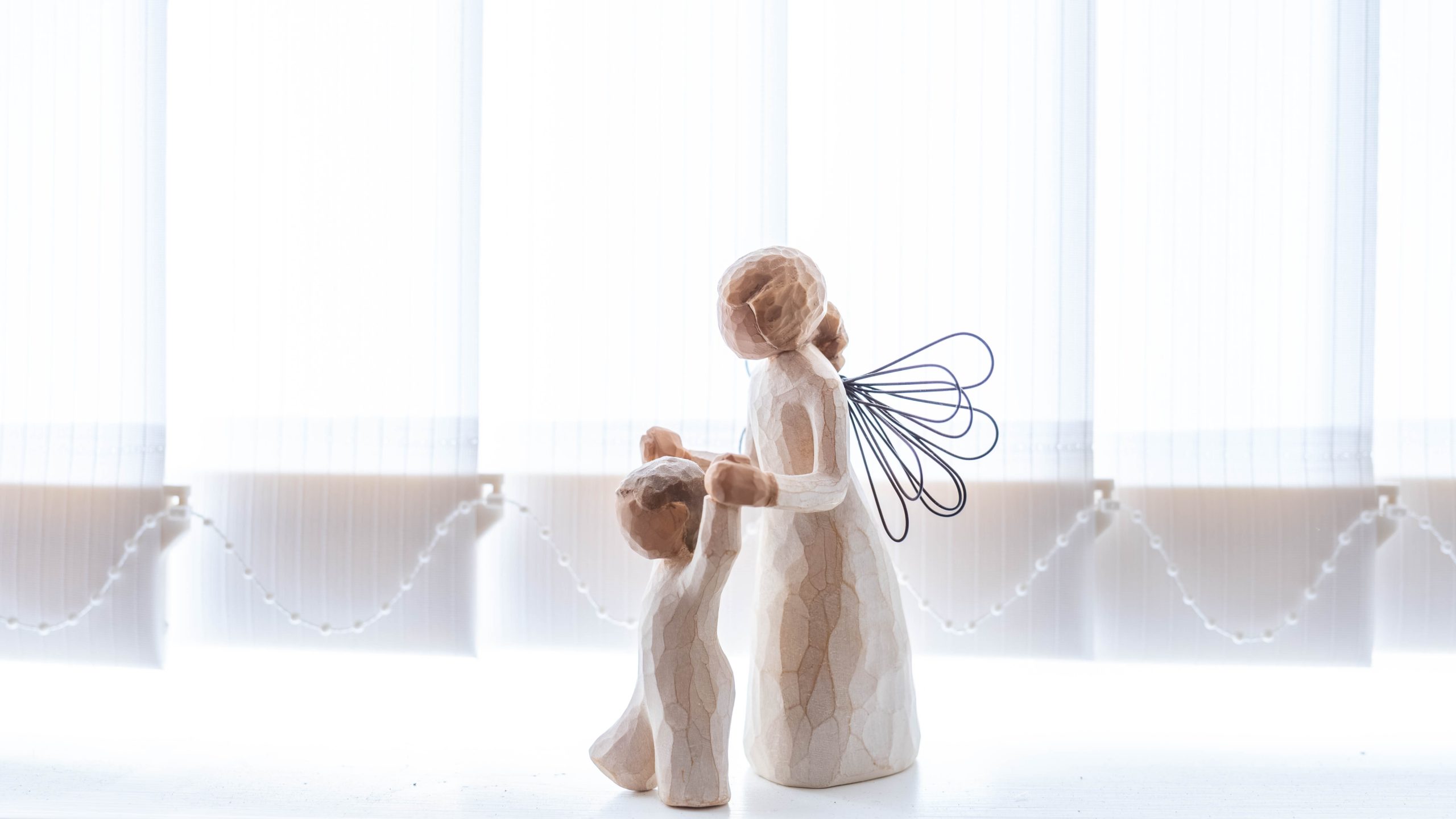 An angel figurine holding the hands of a child figurine supporting them