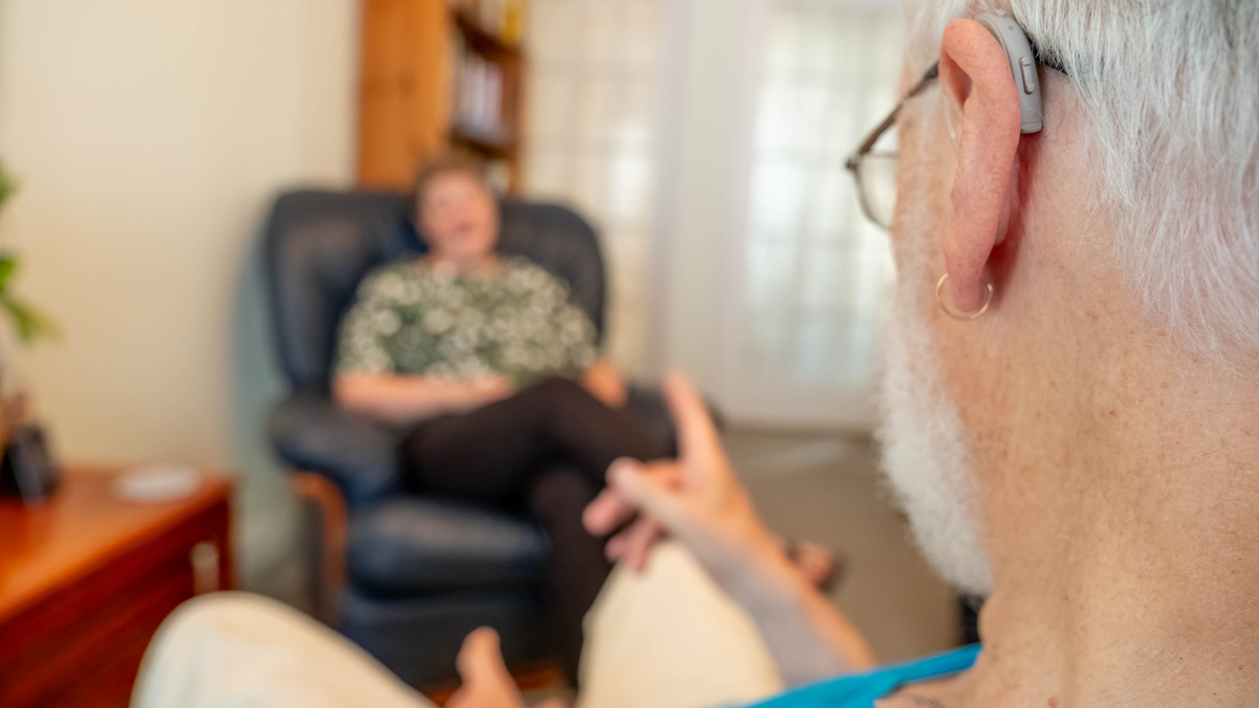 A male from the back of their head, with Annie seated opposite, out of focus, and the male lifts an accusatory finger